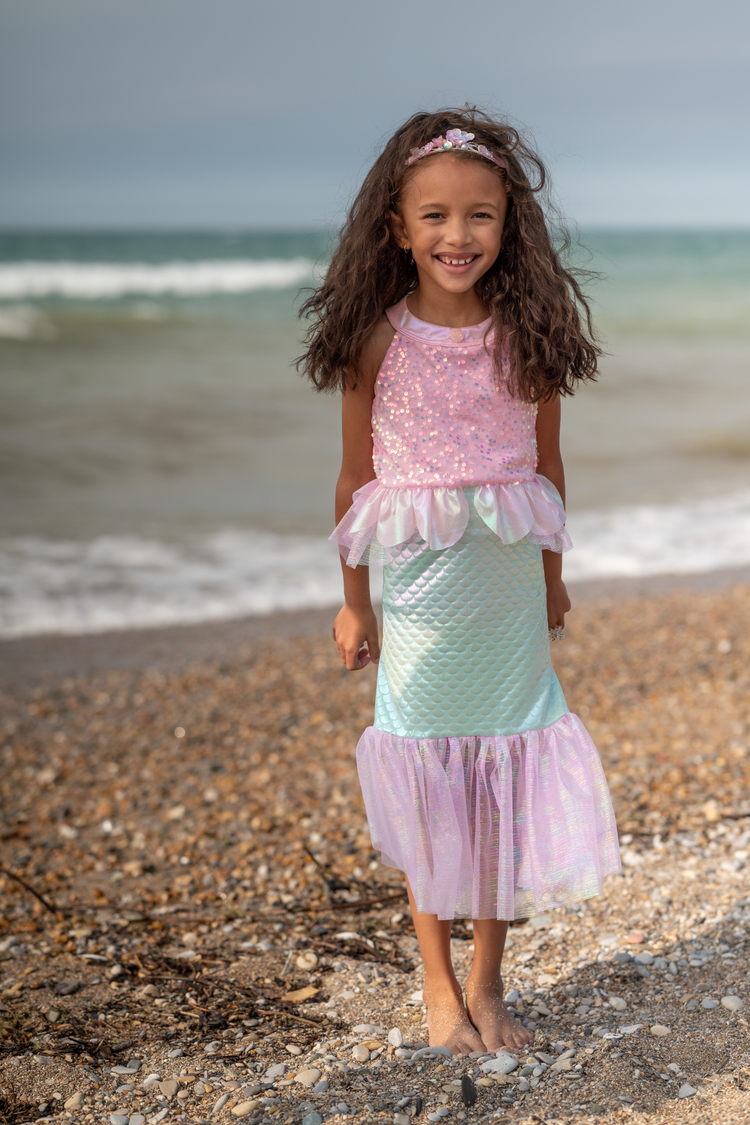 Young girl wearing pink sequin and mint blue mermaid costume dress on sandy beach