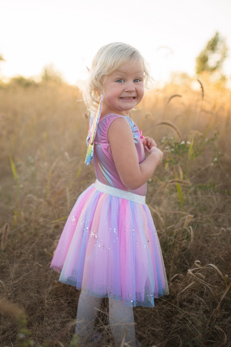 Young girl wearing rainbow sequin tutu skirt with colorful wings in golden field