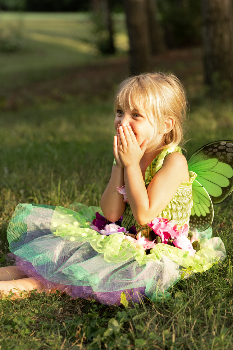 Young girl wearing green fairy costume dress with wings and floral accents outdoors