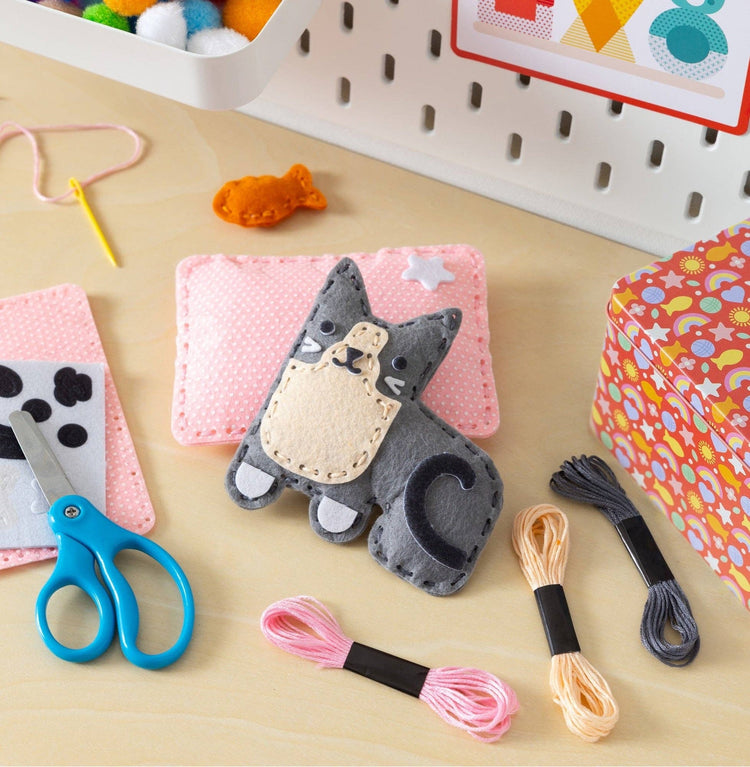 Mini craft kit with handmade felt gray kitten on pink pillow, scissors, thread, and accessories