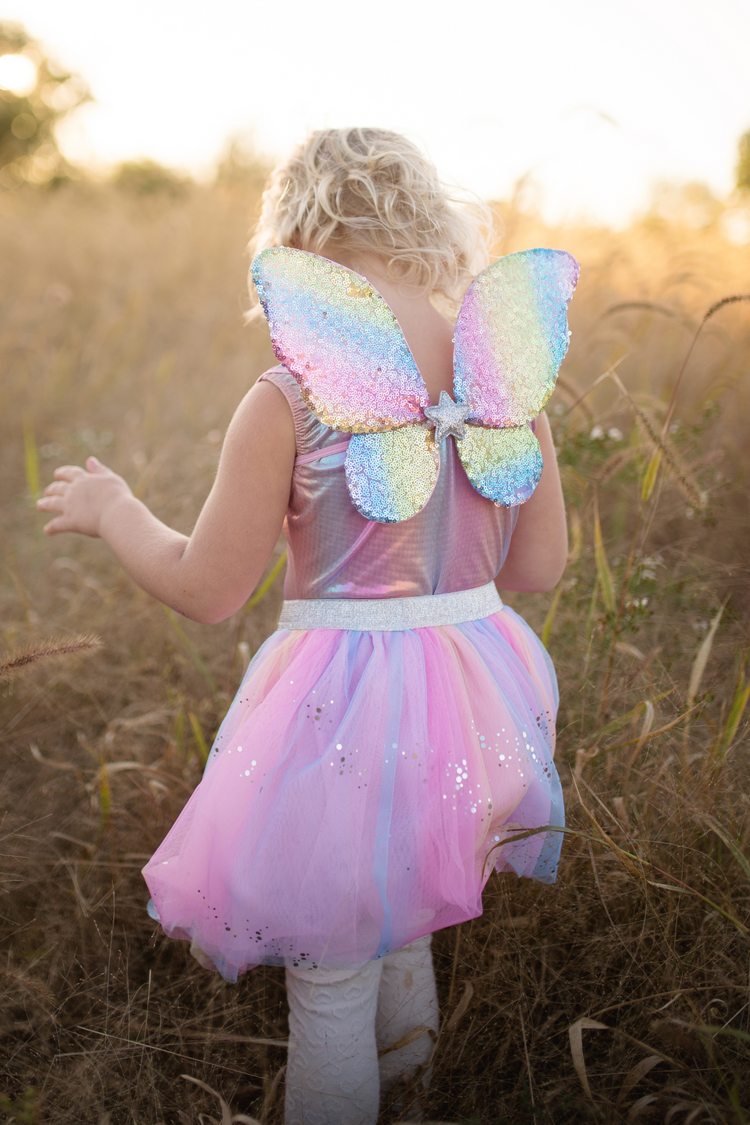 Child wearing rainbow sequin fairy costume with butterfly wings and pink tulle skirt in golden field