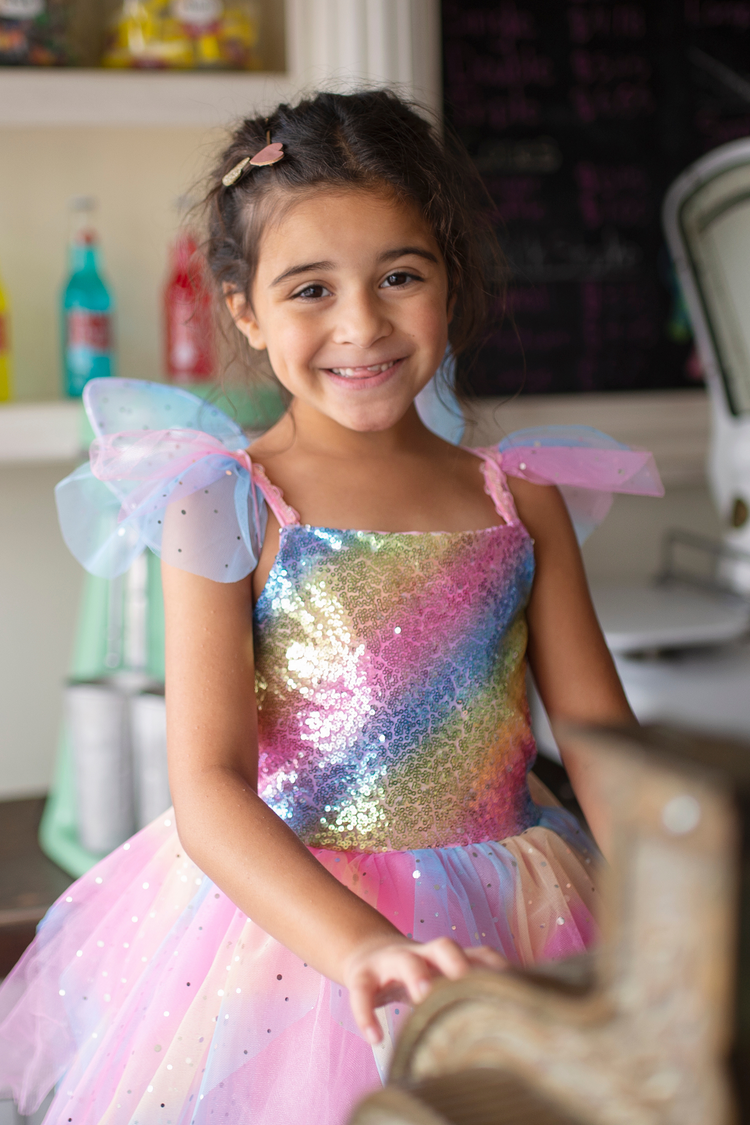 Young girl smiling wearing rainbow sequin fairy dress with colorful tulle wings and skirt