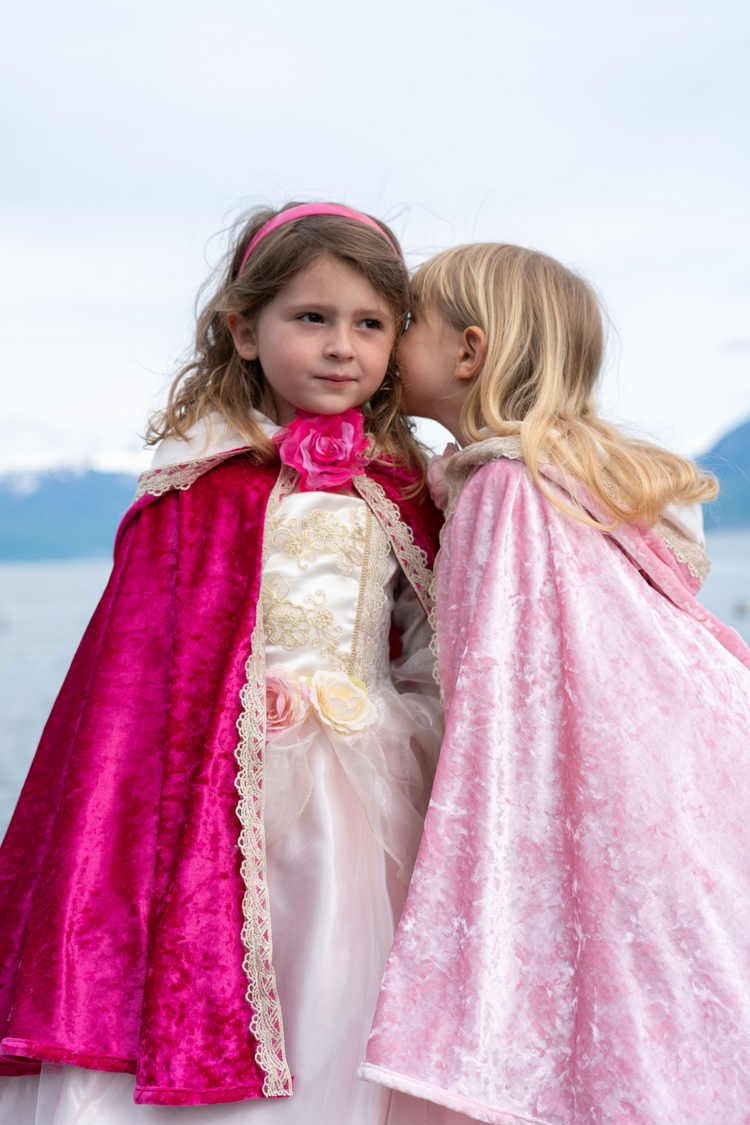 Child wearing a deluxe light pink velvet princess cape with lace trim outdoors near water