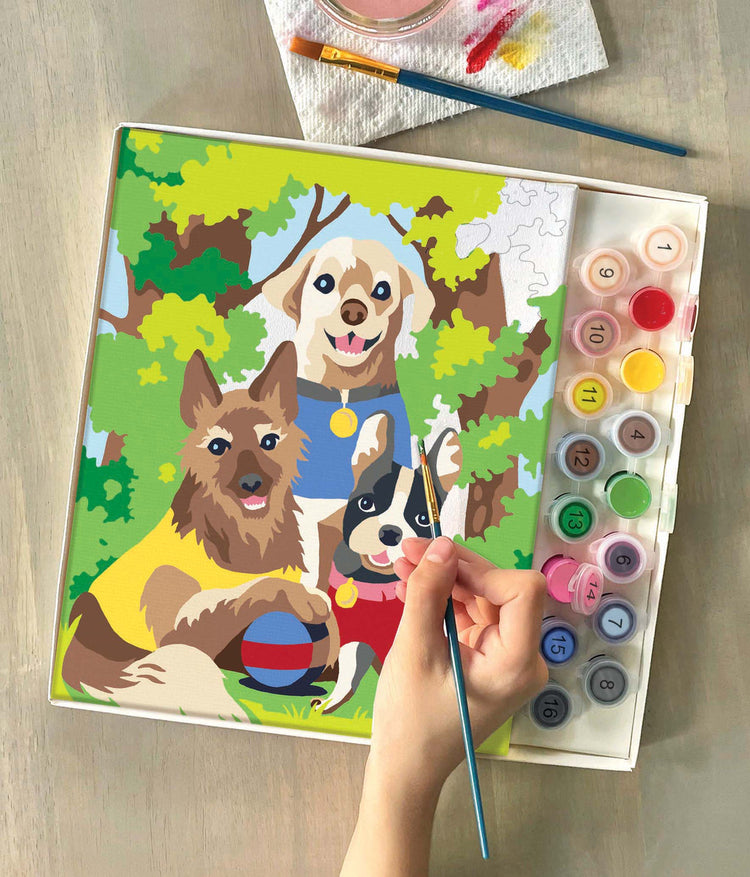 Child painting Dogs Day Out paint by number kit featuring three cartoon dogs outdoors.