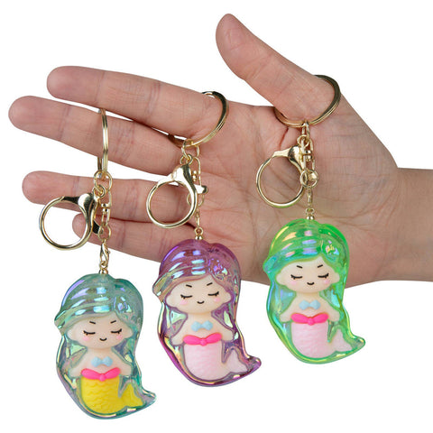 Three iridescent mermaid keychain charms in teal, purple, and green held in a hand