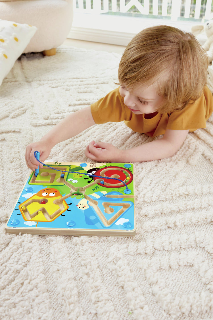 Young toddler lying on carpet playing with Hape Best Bugs Magnetic Maze toy board