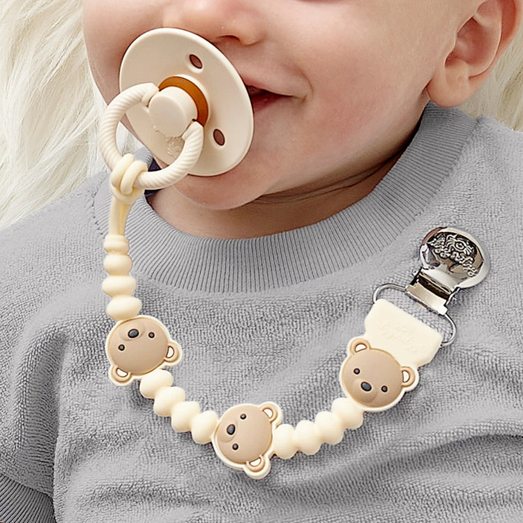 Baby wearing cream Theo the Bear pacifier clip chain attached to gray sweater with pacifier