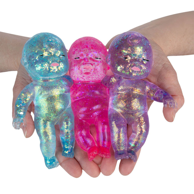 Three glitter-filled translucent baby dolls in blue, pink, and purple held in hands