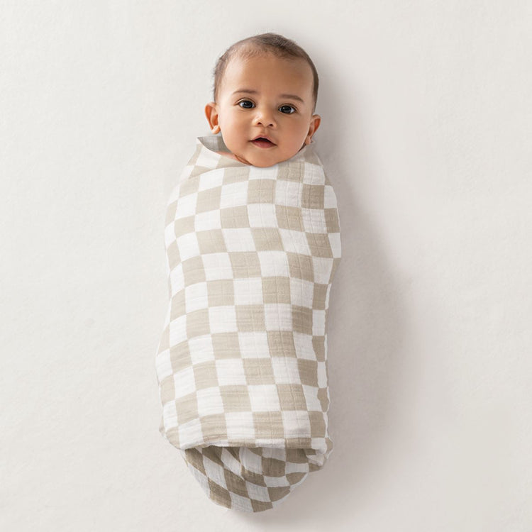 Baby swaddled in taupe and white checkerboard muslin nursing cover on white background
