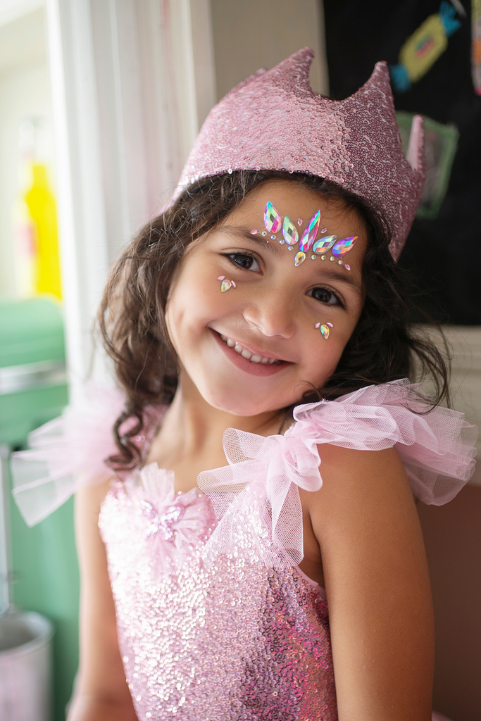 Young girl wearing pink sequin crown and pink unicorn face crystal gems smiling