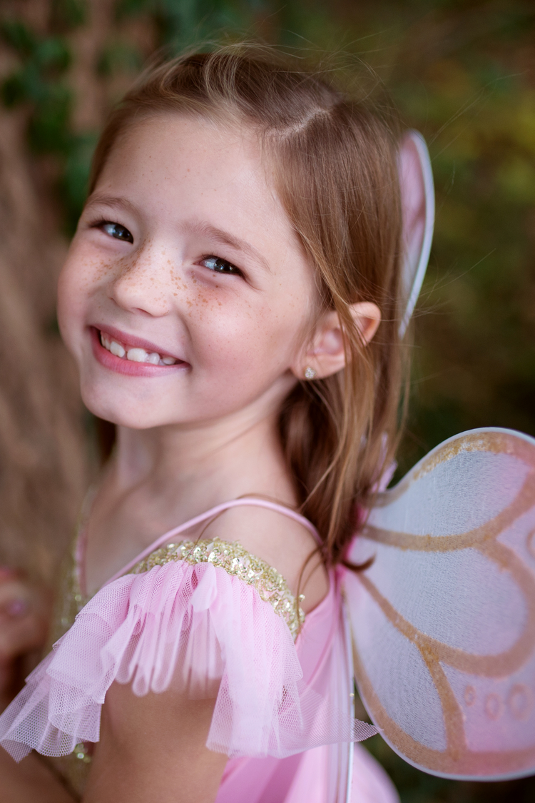 Young girl smiling wearing pink gold butterfly fairy dress with white and gold wings