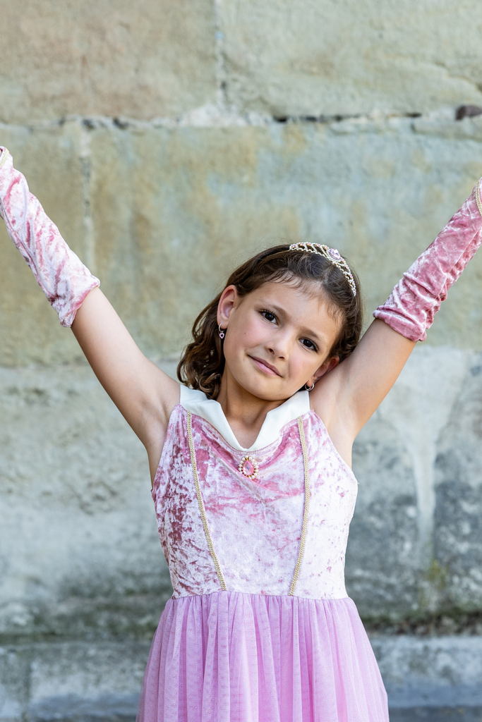 Young girl wearing pink velvet princess gown with matching arm warmers and tiara, arms raised