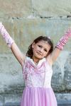 Young girl wearing pink velvet princess gown with matching arm warmers and tiara, arms raised