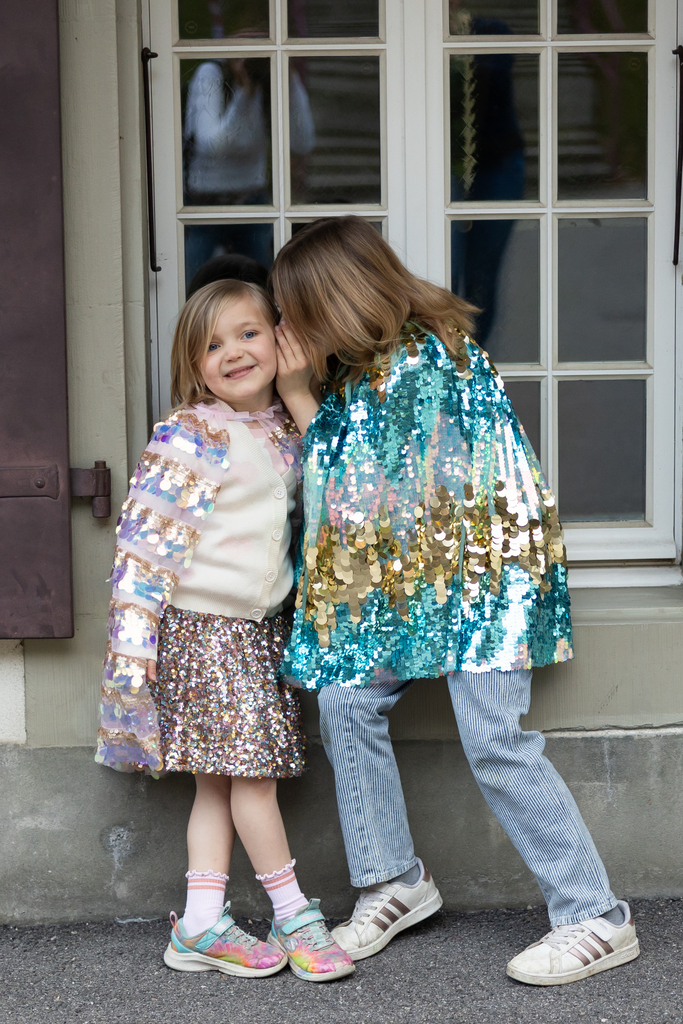 Child wearing gold and light pink iridescent paillette cape over sparkly outfit outdoors