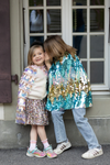 Child wearing gold and light pink iridescent paillette cape over sparkly outfit outdoors