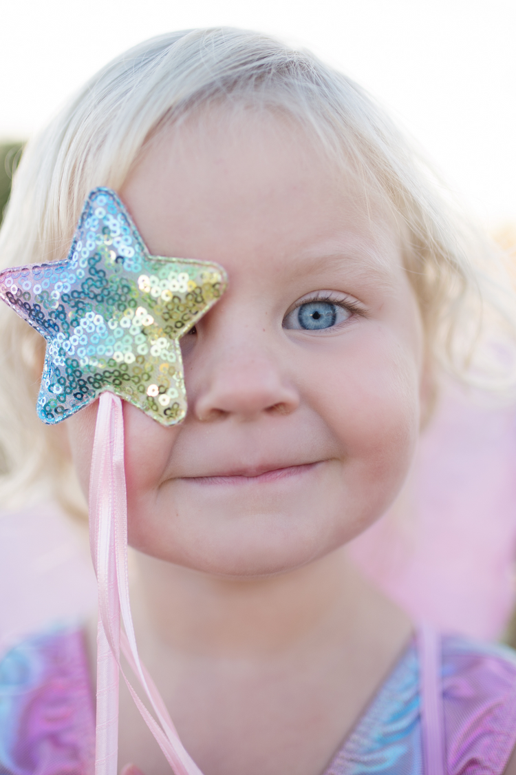 Young girl holding rainbow sequin star wand in front of her eye, smiling