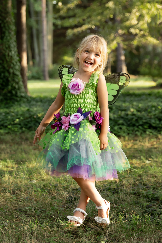 Young girl wearing green fairy costume dress with butterfly wings and floral accents outdoors
