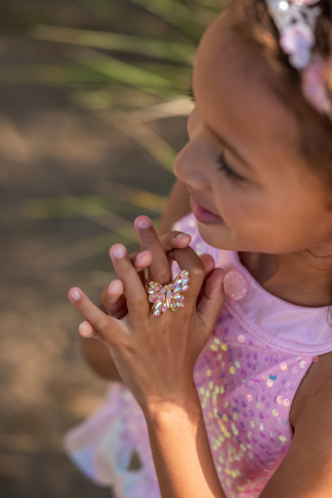 Young girl wearing iridescent butterfly ring with rainbow gemstones on her finger