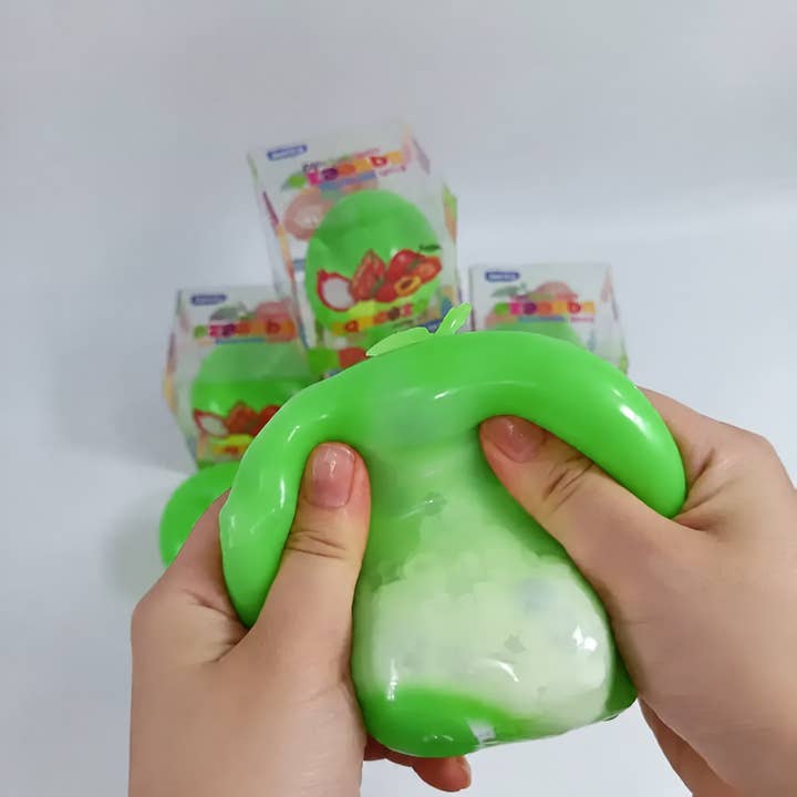 Hands squishing a green apple-shaped squishy toy with white foam interior visible