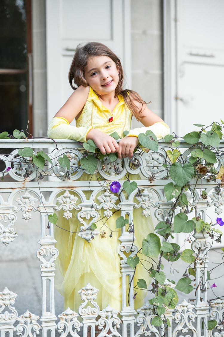 Young girl wearing yellow princess gown with arm warmers on decorative balcony