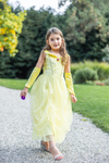 Young girl wearing yellow princess gown with velvet arm warmers walking outdoors on garden path