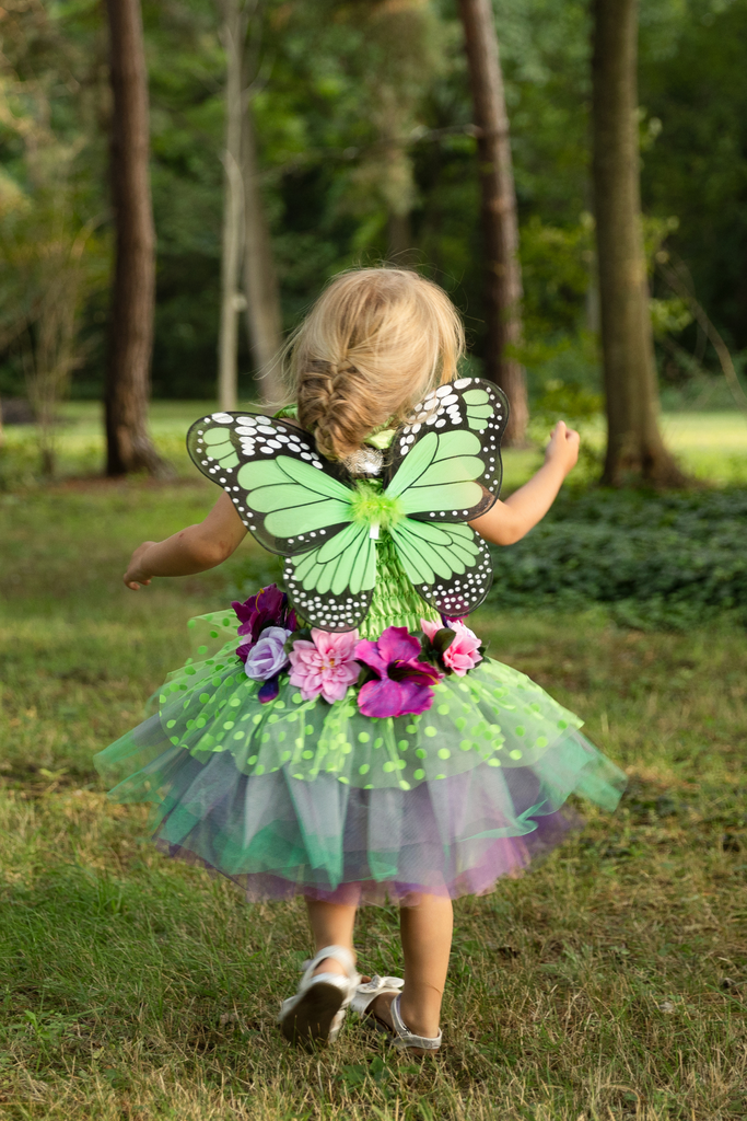 Toddler girl wearing green fairy butterfly wings dress with floral accents outdoors