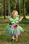 Toddler girl wearing green fairy butterfly wings dress with floral accents outdoors