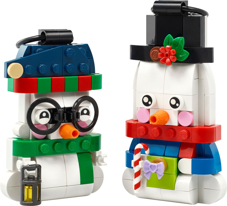 Two LEGO snowman ornaments with top hats, scarves, carrot noses, and holiday accessories on white background.