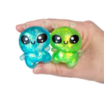 Hand holding two sparkly alien squeeze toys in blue and green glitter colors
