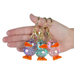 Three iridescent duck keychains in purple, teal, and pink held in a hand showing size.