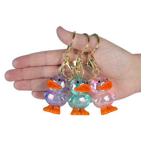 Three iridescent duck keychains in purple, teal, and pink held in a hand showing size.
