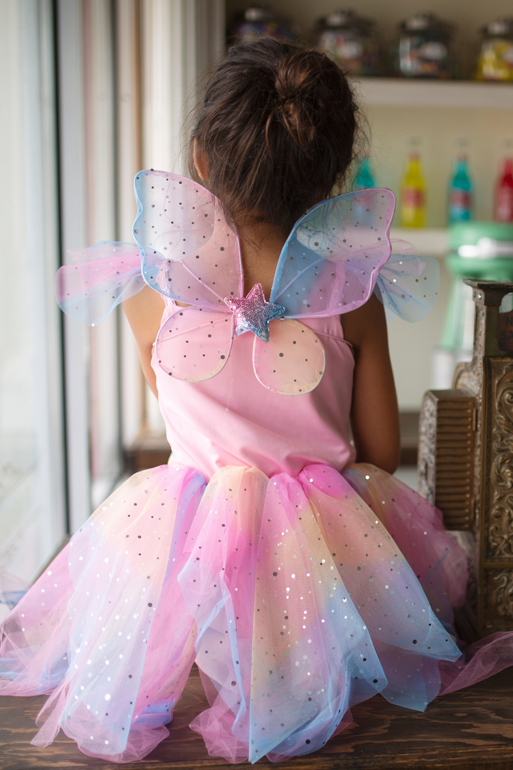 Child wearing rainbow fairy costume dress with pastel tutu skirt and butterfly wings