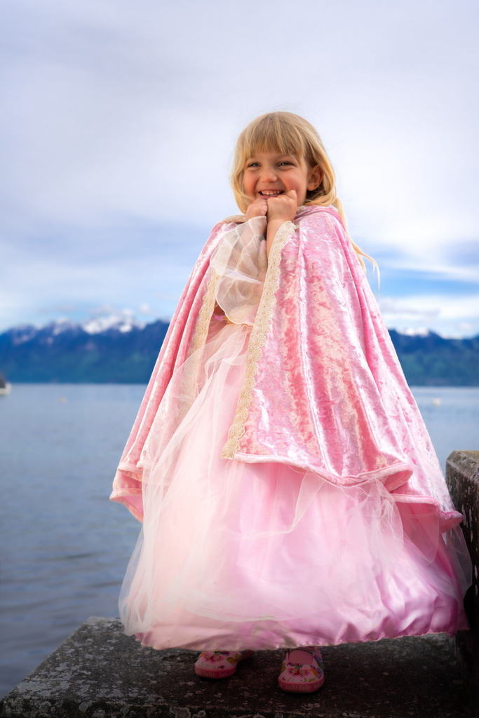 Young girl wearing a deluxe pink velvet princess cape with gold lace trim and tulle dress outdoors.