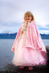 Young girl wearing a deluxe pink velvet princess cape with gold lace trim and tulle dress outdoors.