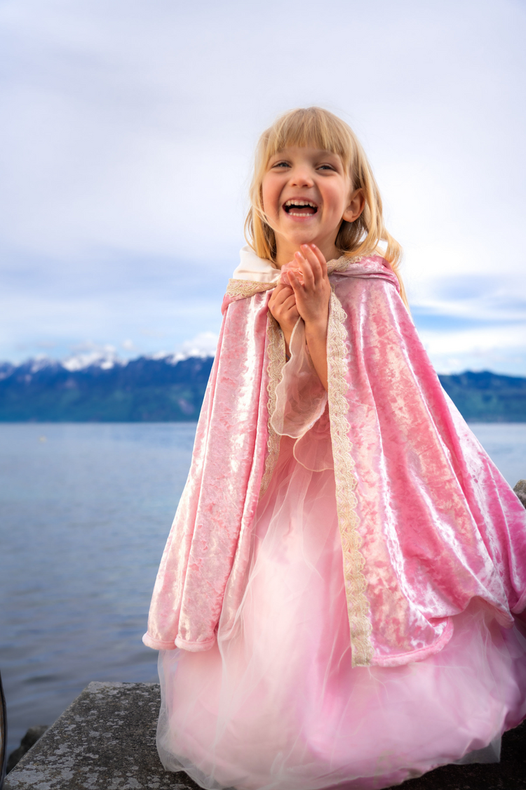 Young girl wearing a deluxe pink velvet princess cape with lace trim outdoors by a lake