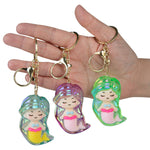 Three iridescent mermaid keychain charms in teal, purple, and green held in a hand