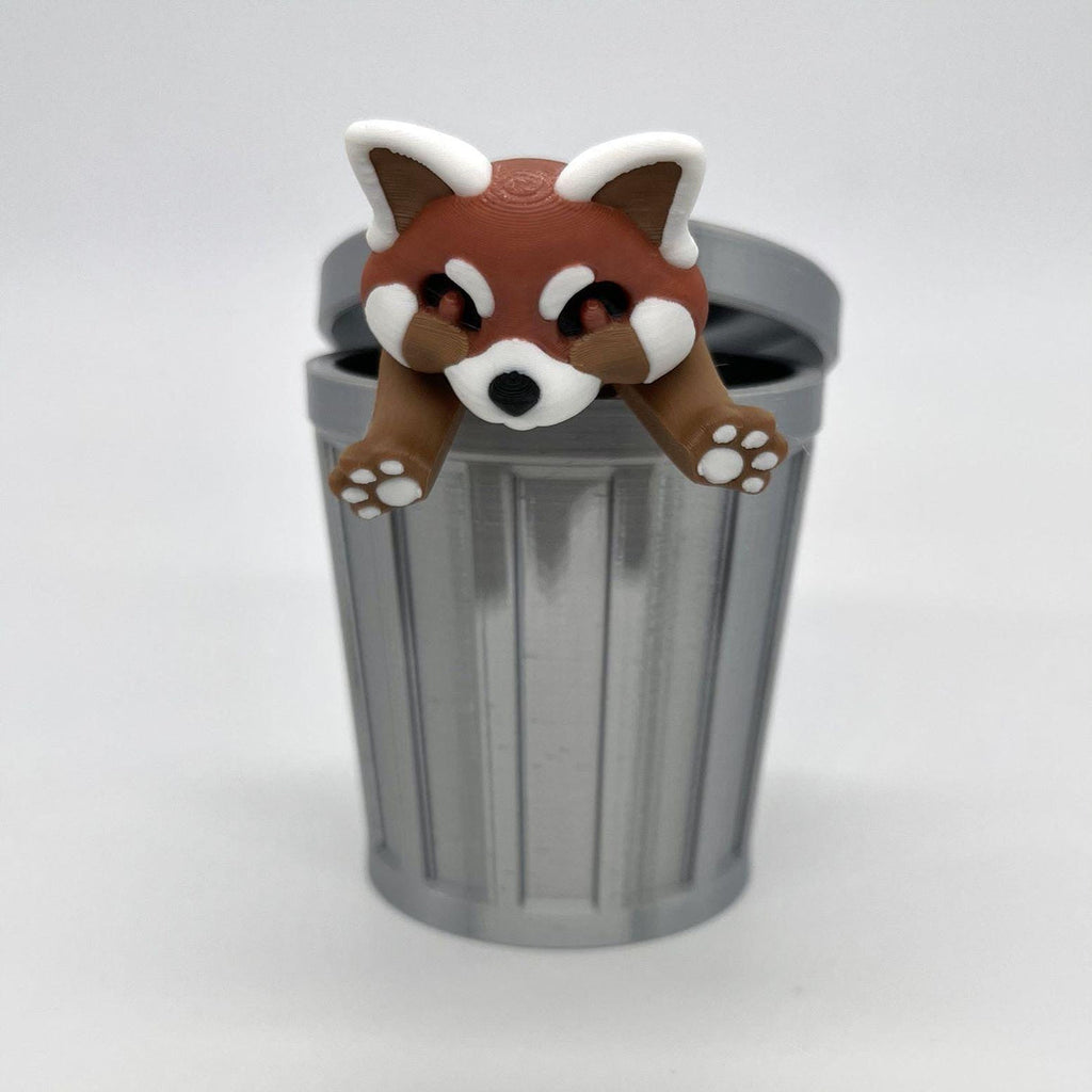 3D printed red panda figure draped over a miniature gray trash can toy