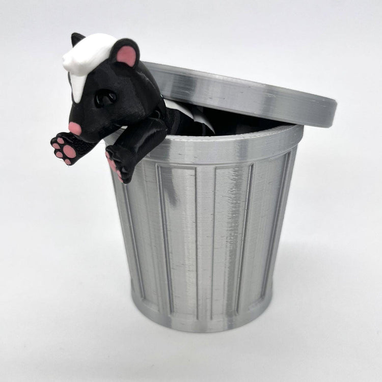 Cute 3D-printed skunk figurine peeking out of a miniature silver trash can toy