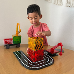 Young child playing with Magna-Tiles Builder 32-piece set featuring translucent magnetic tiles, road tracks, crane, and truck