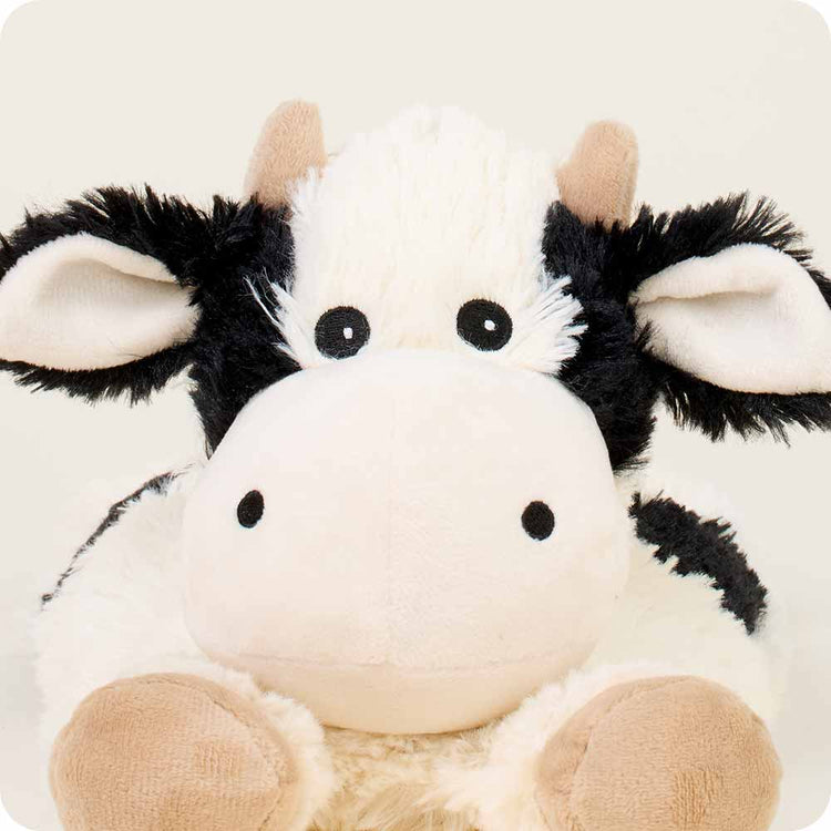 Warmies laying down cow stuffed animal with black and white plush fur and tan hooves
