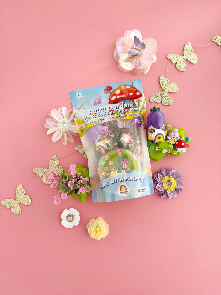 Fairy Garden Mini KidDough Play Pack on pink background surrounded by decorative flowers and glitter butterflies