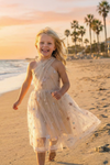 Young girl running on beach wearing champagne tulle dress with colorful star sequins at sunset