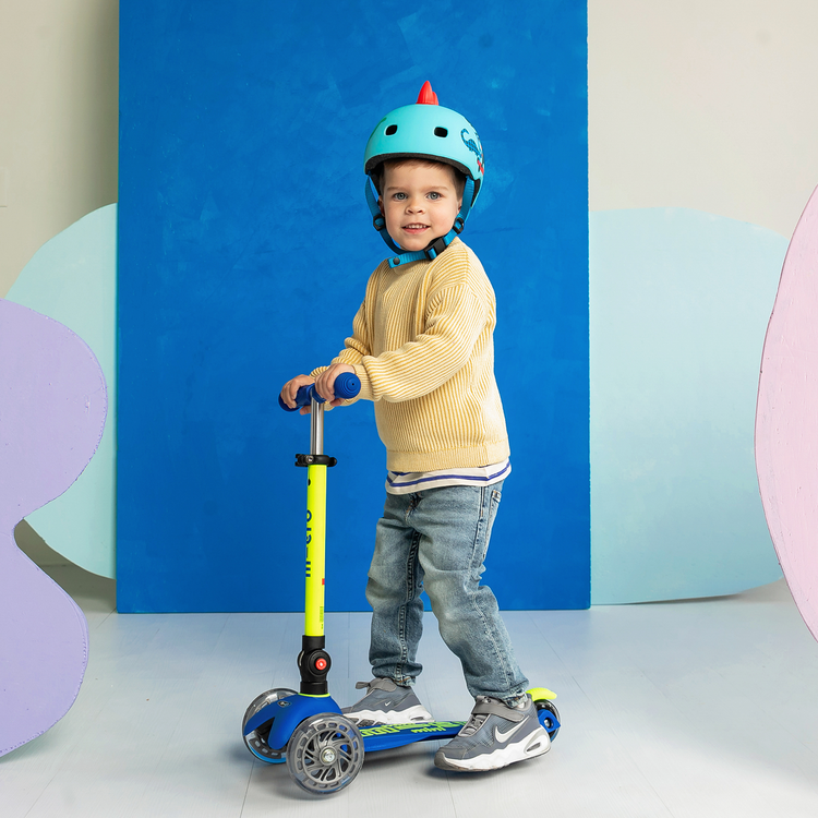 Young child wearing teal helmet riding blue and neon yellow Micro Mini LED scooter