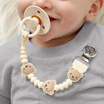 Baby wearing cream Theo the Bear pacifier clip chain attached to gray sweater with pacifier