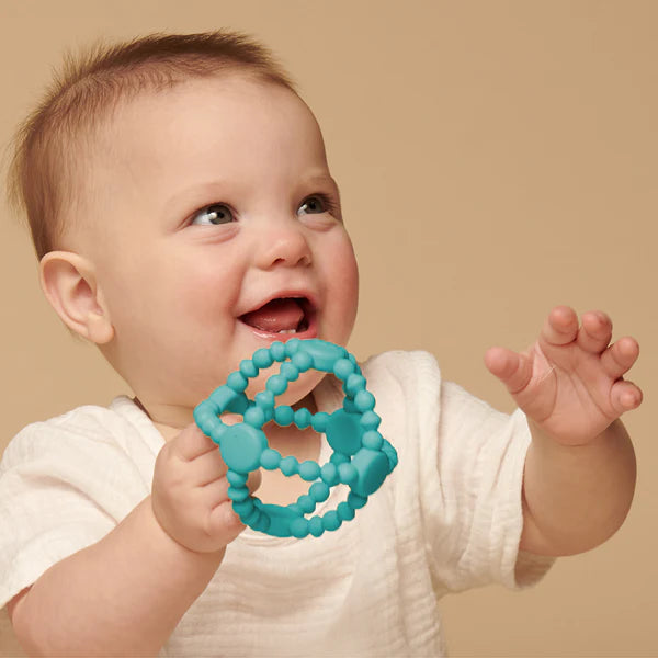 Happy baby holding and chewing on a teal Itzy Ritzy Bitzy Ball silicone teether toy