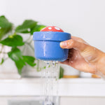 Hand holding blue mushroom-shaped bath toy pouring water streams from bottom