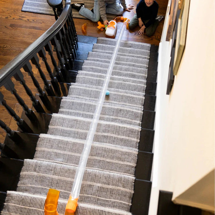 Two children playing with Air Toobz tube toy set running down carpeted staircase at home.