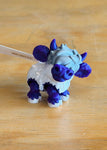 3D printed Frostbite Flurry Micro Moos cow figurine in blue, purple, and white on wooden surface