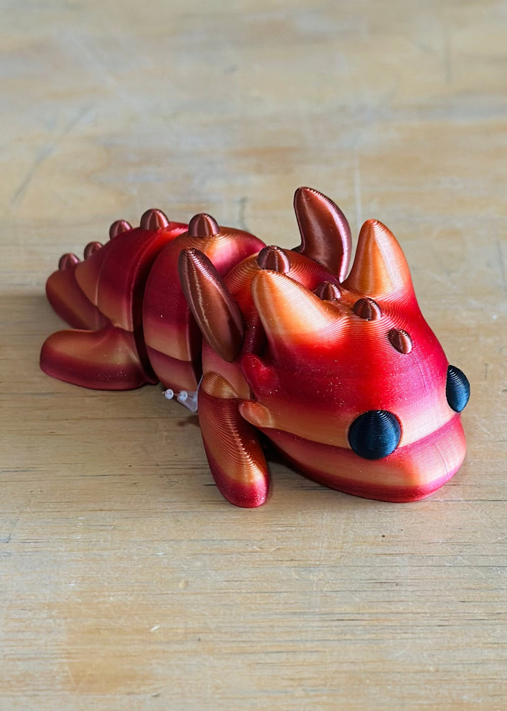 Red and orange metallic 3D-printed articulated winged dragon toy on wooden surface