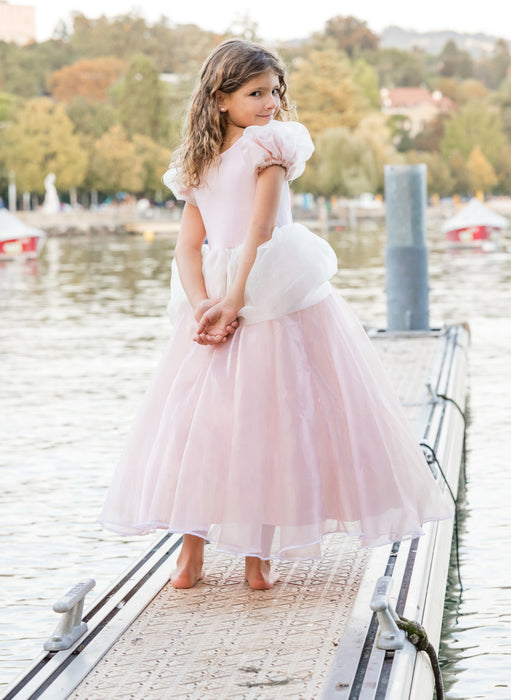Young girl wearing light pink tulle princess gown with puff sleeves on a dock
